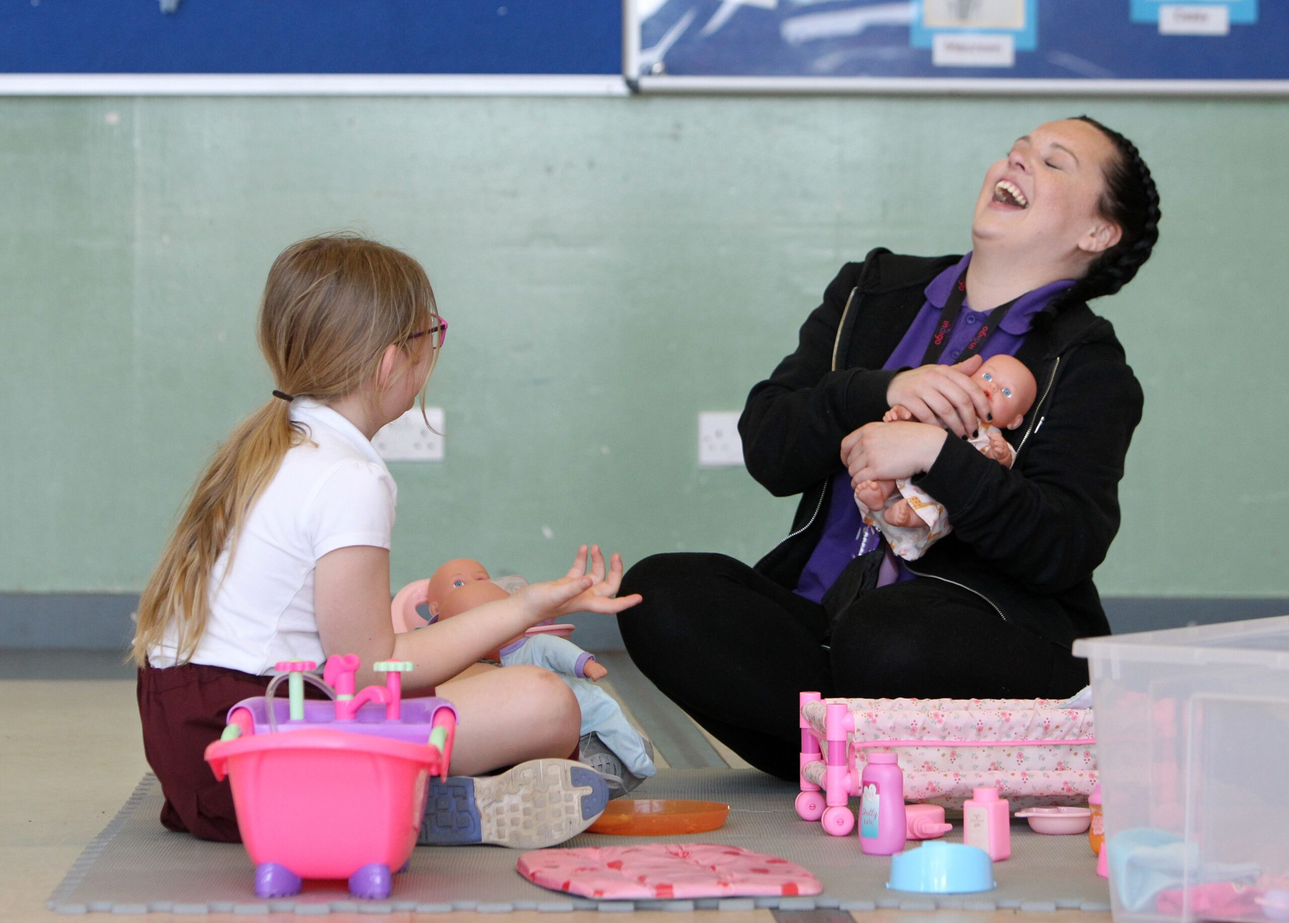 a young girl and employee sitting on the floor playing with dolls