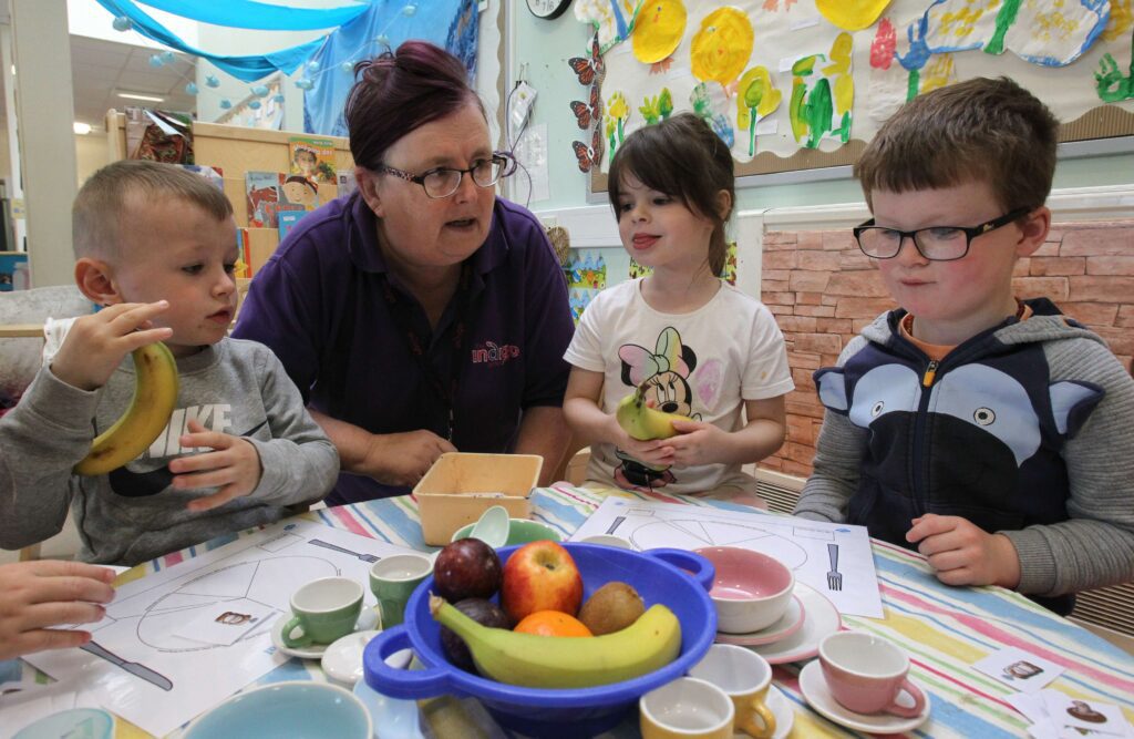 Children sitting at a table with fruit being supervised by a staff member