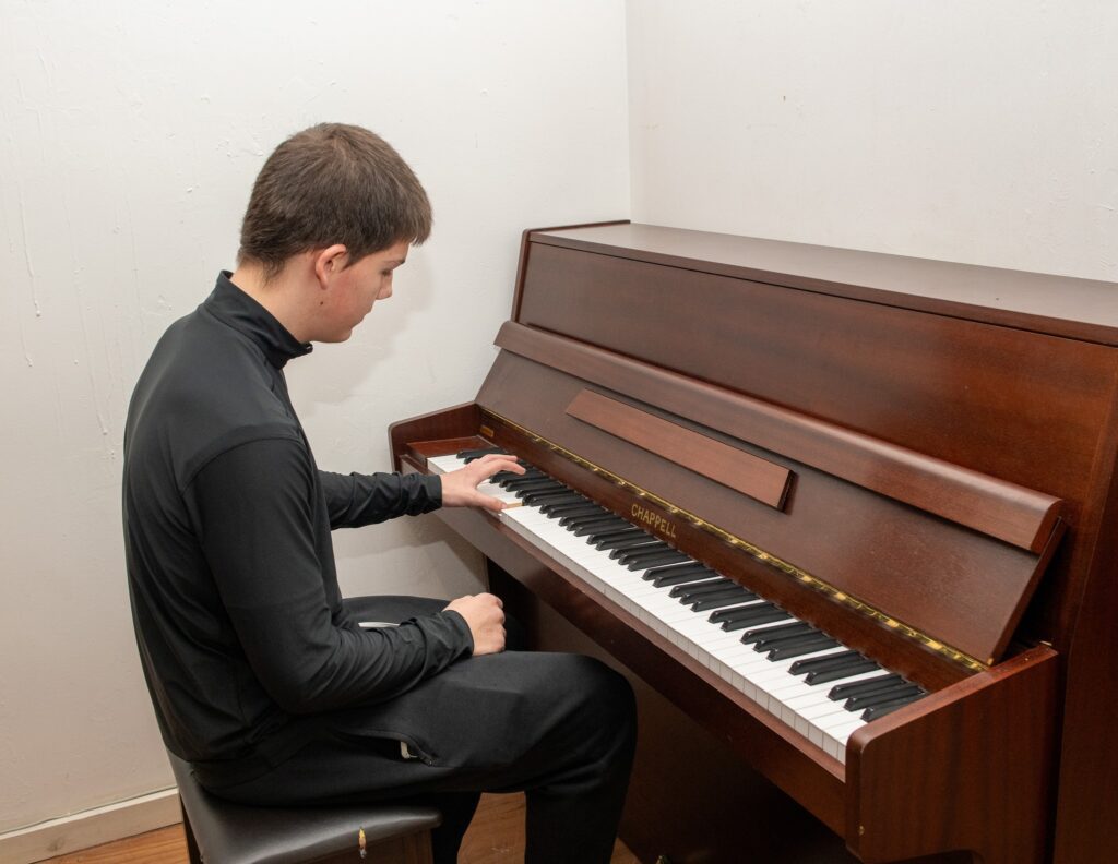 A teenager in a black polo shirt and black trousers playing the piano