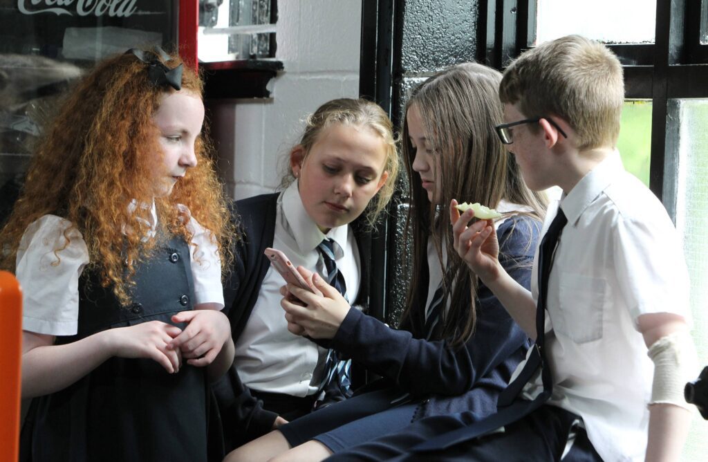 Several schoolchildren wearing uniforms are sitting together inside a building, and talking to each other.