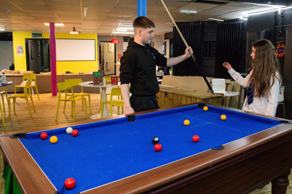 Two teenagers are playing pool. One is dressed in black clothes, and the other is wearing a school uniform