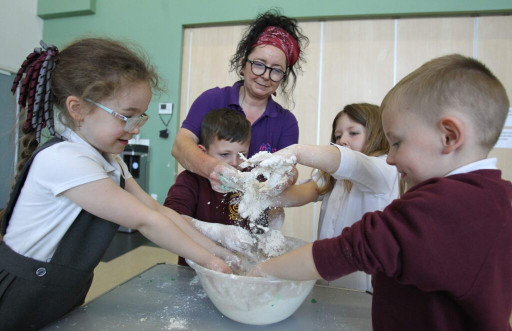 A group of children playing with a ball of dough and flower supervised by a staff member