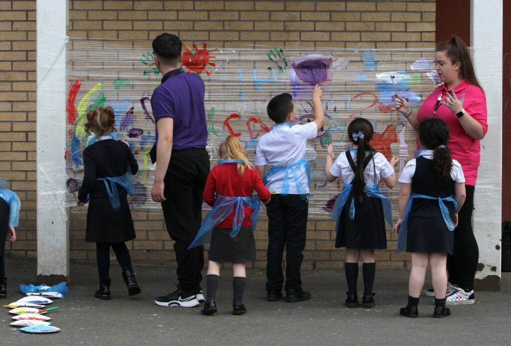 Children under the supervision of an employee painting on clear plastic outside