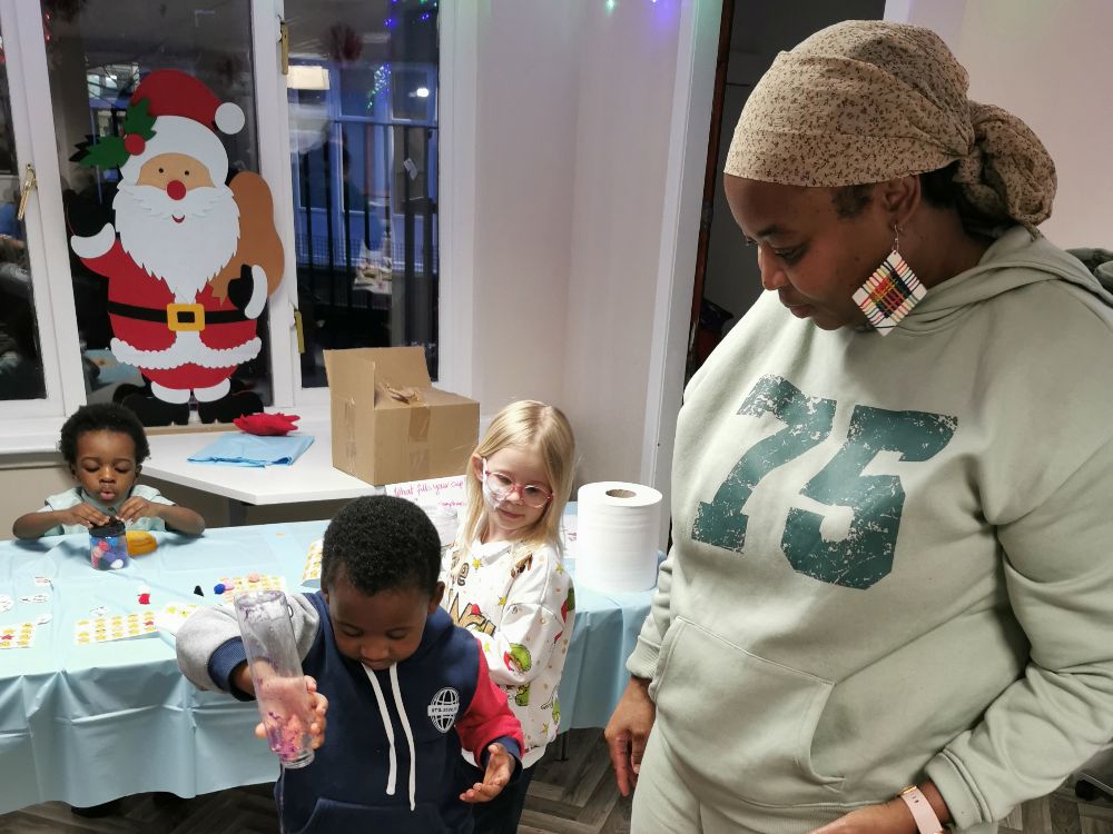 During a Family Matters activity, a person wearing a sports suit is in the foreground, while two small children in sports clothes are sitting at a table in the background